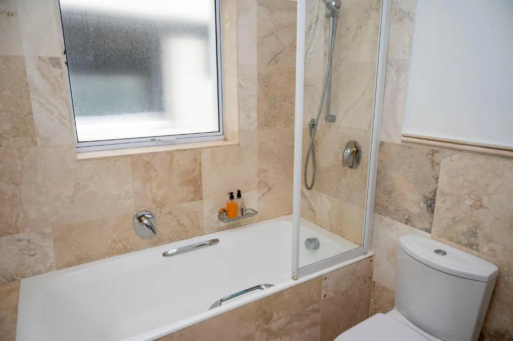 Cream travertine bathroom with bathtub, shower enclosure, and toilet