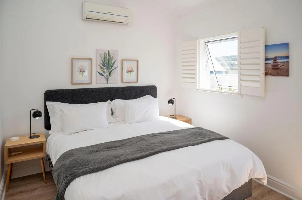 Bright bedroom with queen bed, black headboard, white linens, and waterfront view through shuttered window