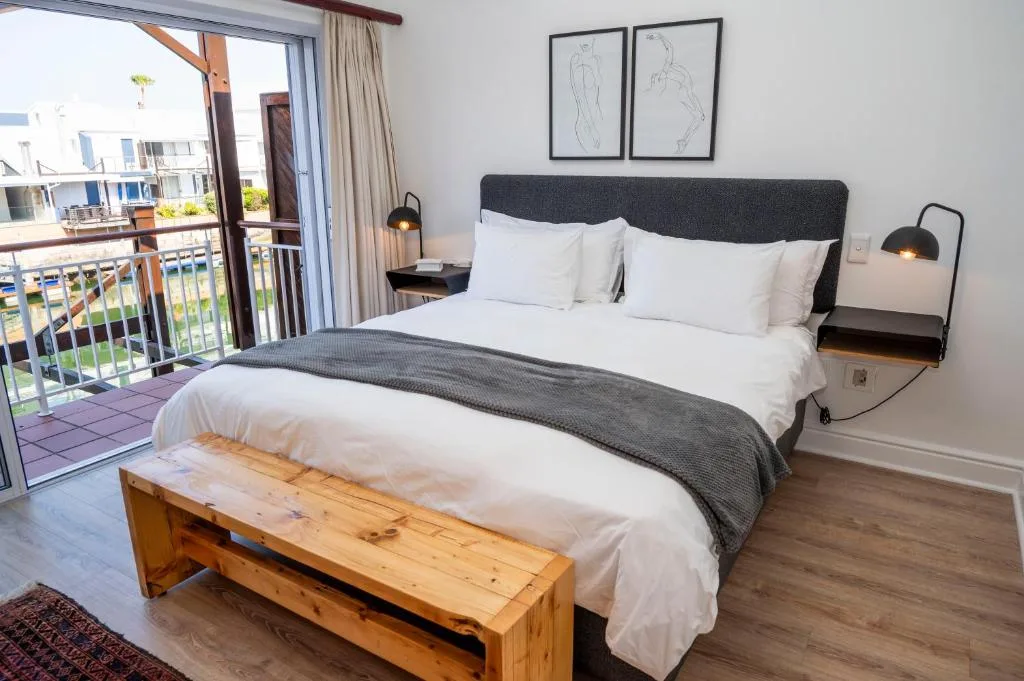 Modern bedroom with queen bed, white linens, and balcony overlooking waterfront