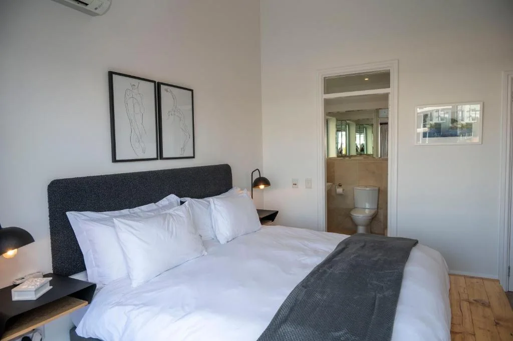 Modern bedroom with dark headboard, white linens, ensuite bathroom visible