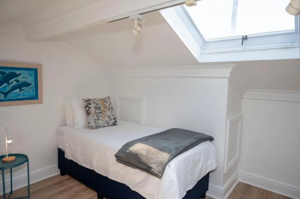 Bright attic bedroom with skylight, white bedding, and coastal artwork