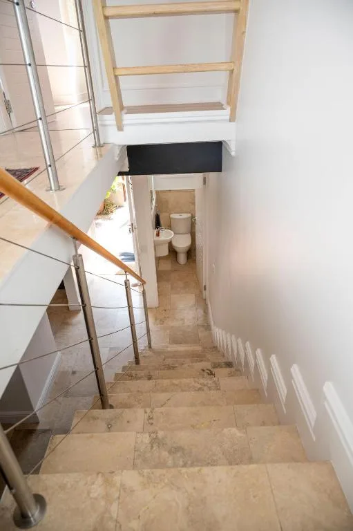 Staircase with wooden railing leading down to bathroom entrance