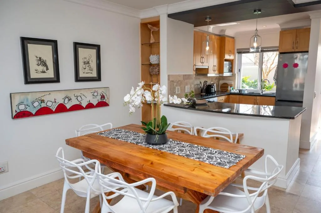 Wooden dining table with white chairs, kitchen visible behind