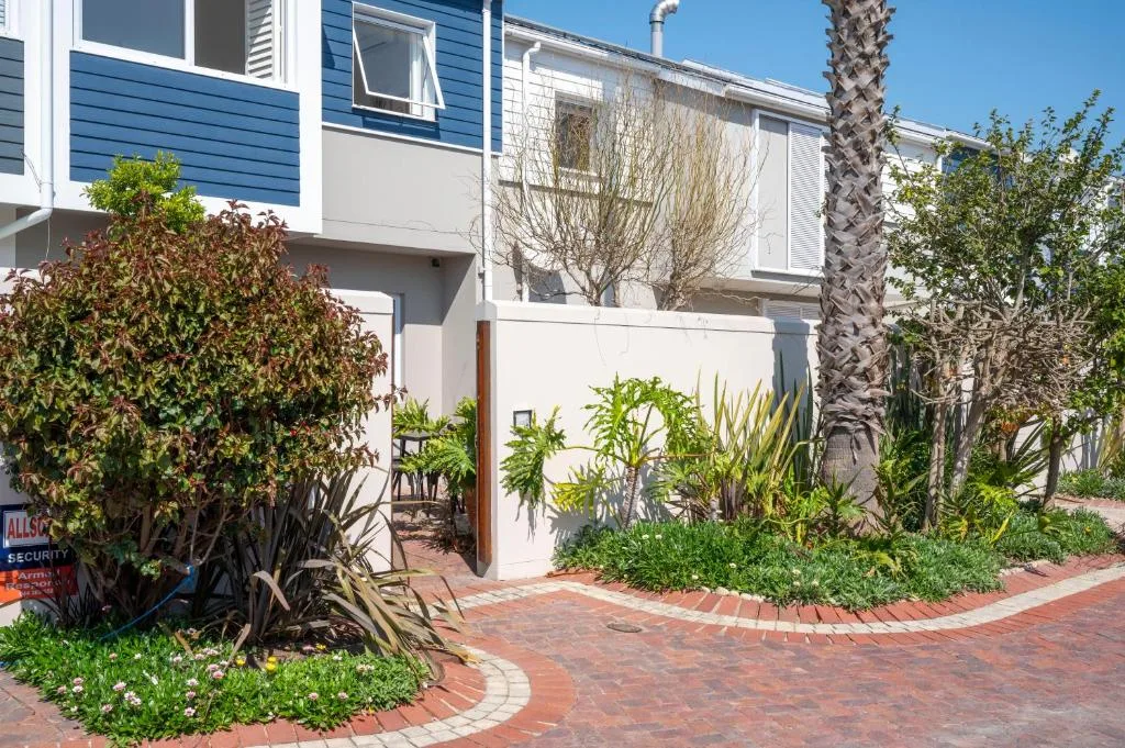 Modern white house facade with blue trim, tropical plants, and brick pathway