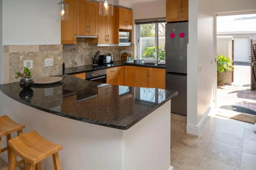 Modern kitchen with wooden cabinetry, dark granite countertops, and stainless steel appliances