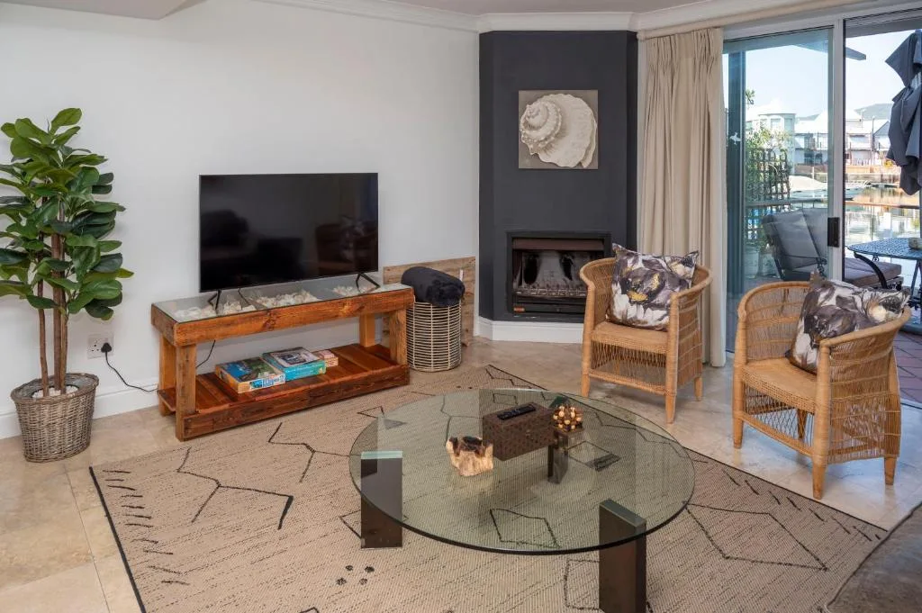 Modern lounge with fireplace, TV, wicker chairs, and deck views