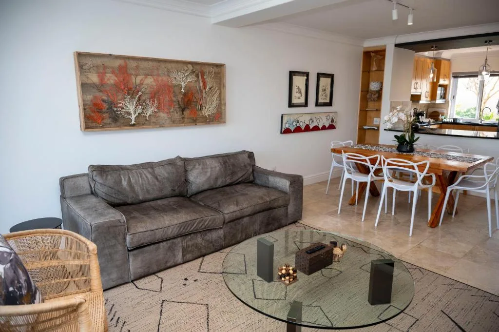 Modern living room with gray sofa, glass coffee table, and dining area beyond