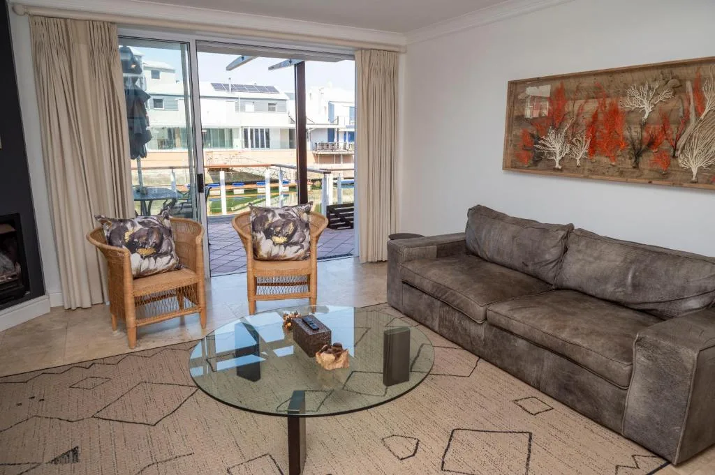 Spacious lounge with gray sofa, wooden chairs, glass coffee table, and waterfront views