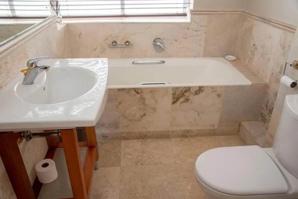 Marble bathroom with sunken bathtub, round sink, and toilet fixtures