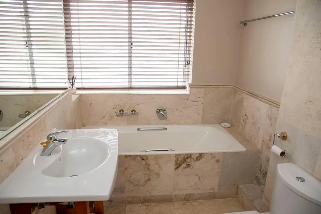 Marble bathroom with bathtub, sink, toilet, and bright window blinds