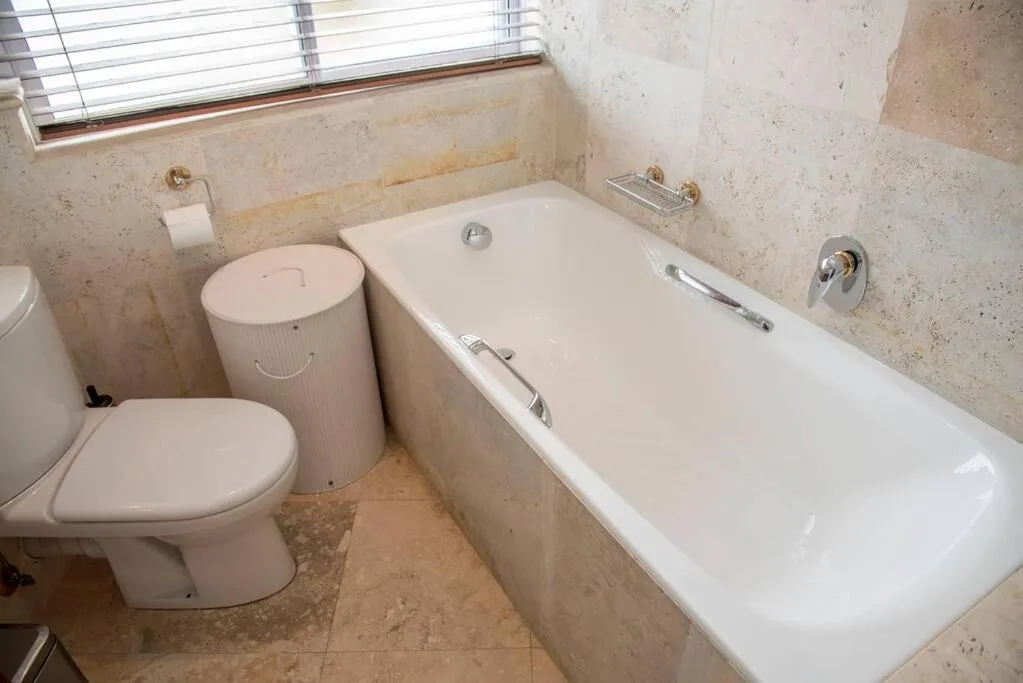 Bathroom with toilet, bathtub, and travertine tile walls with window