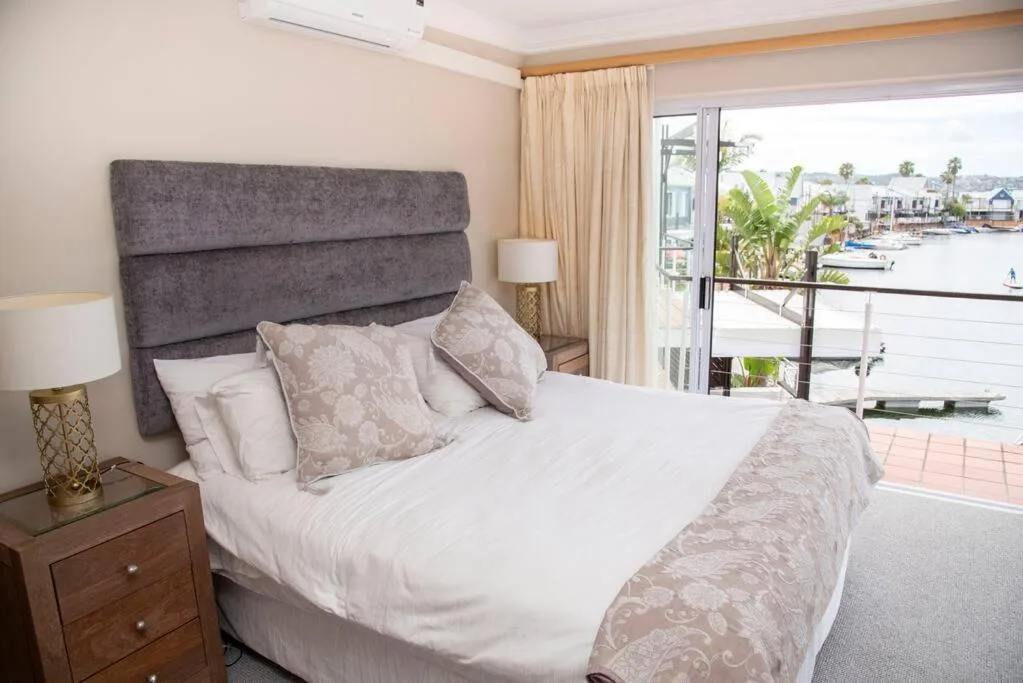Spacious bedroom with grey upholstered headboard and waterfront view through glass doors