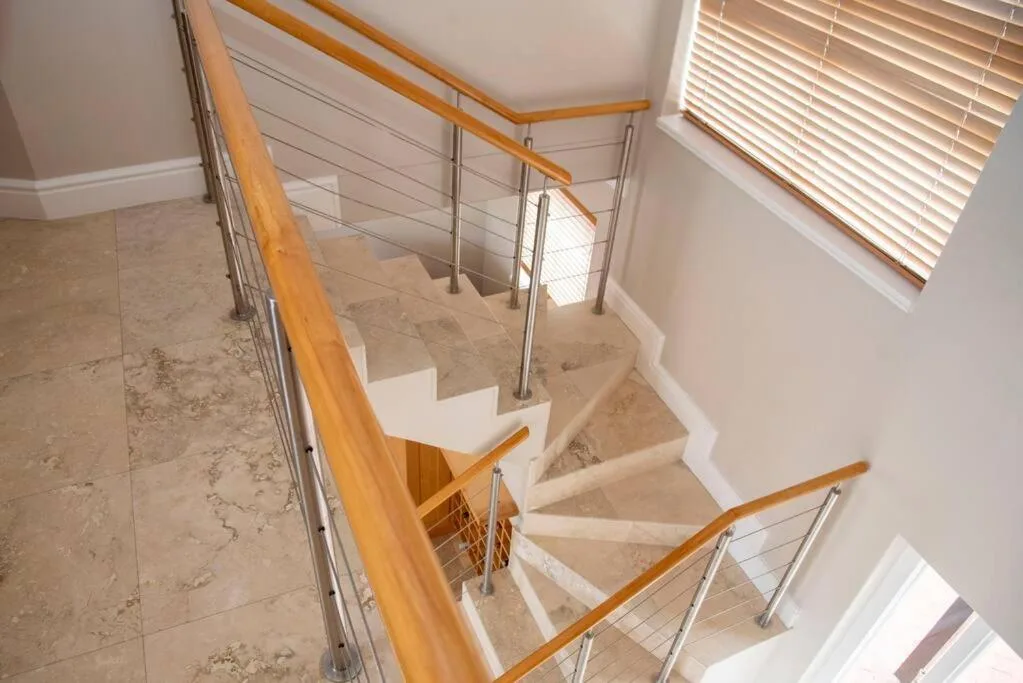 Modern staircase with wooden handrail and stainless steel cable railing