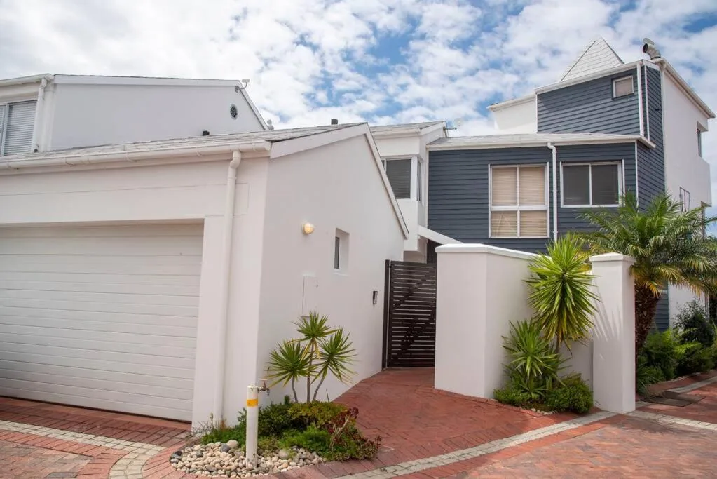 Modern white and blue house with garage, brick driveway, and tropical plants