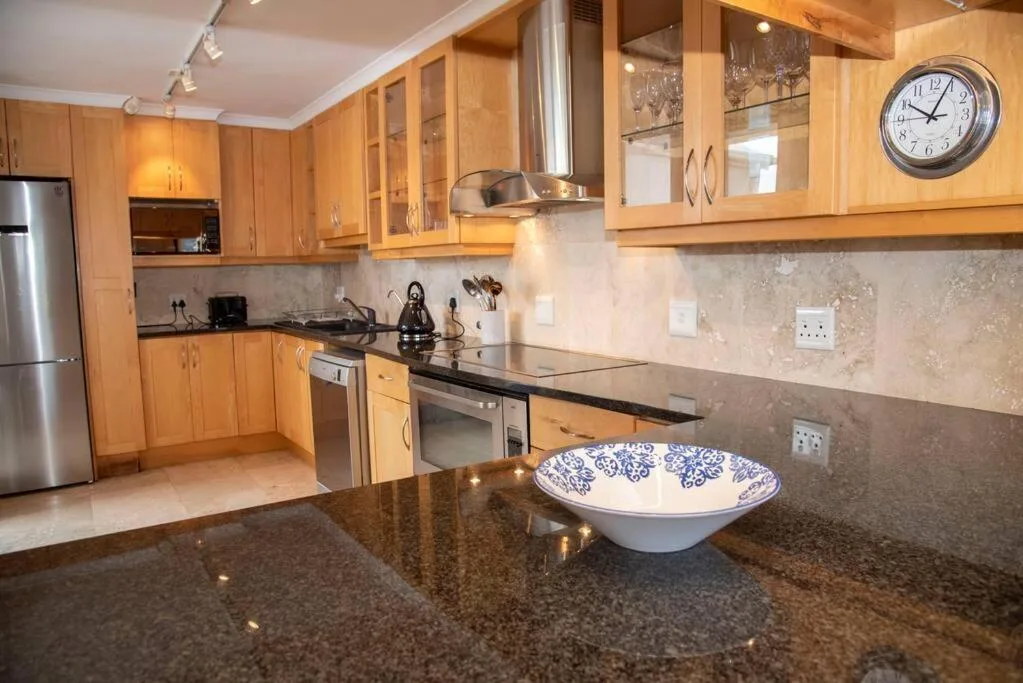 Modern kitchen with wooden cabinetry, stainless steel appliances, dark granite countertops
