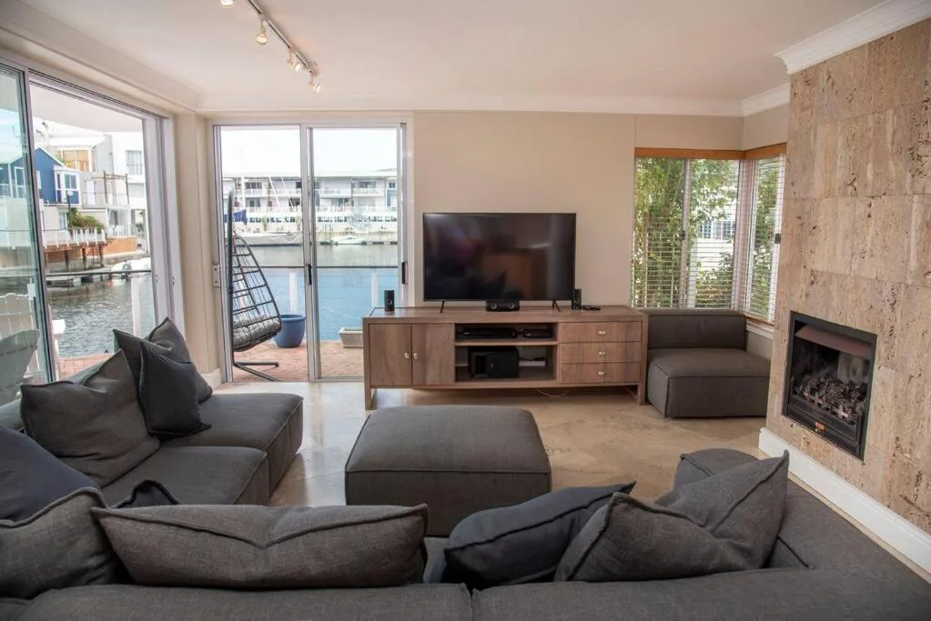 Spacious waterfront lounge with dark sofas, fireplace, and water views