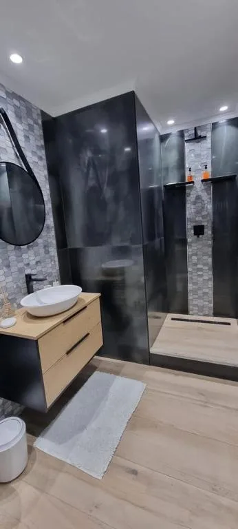 Modern bathroom with black shower enclosure, wooden vanity, round mirror