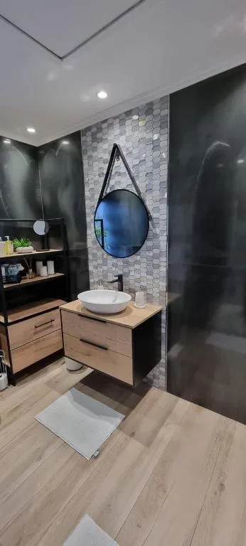 Modern bathroom with round blue mirror, vessel sink, and tiled accent wall
