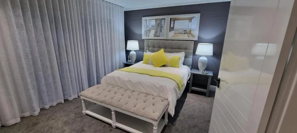 Modern bedroom with yellow accent pillows, neutral bedding, and dark feature wall