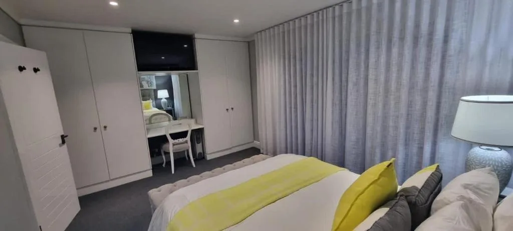 Modern bedroom with yellow accents, desk area, and floor-to-ceiling curtains