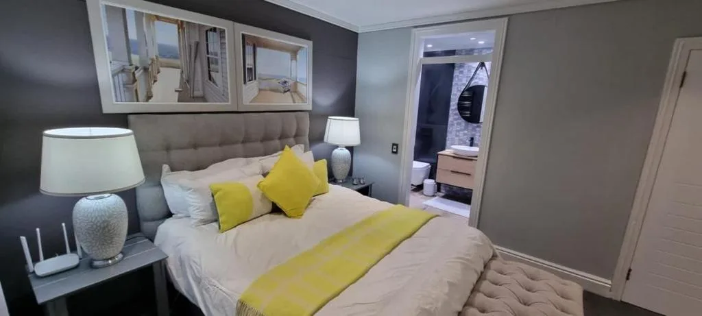 Modern bedroom with queen bed, yellow accents, and en-suite bathroom visible
