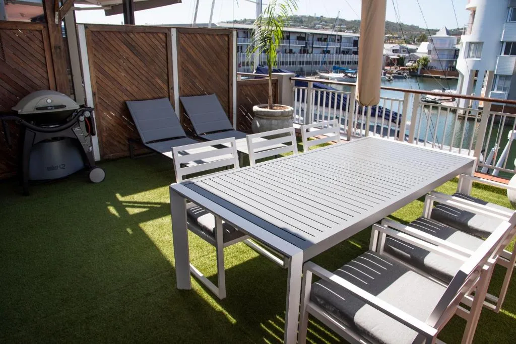 Waterfront deck with dining table, loungers, braai, and canal views