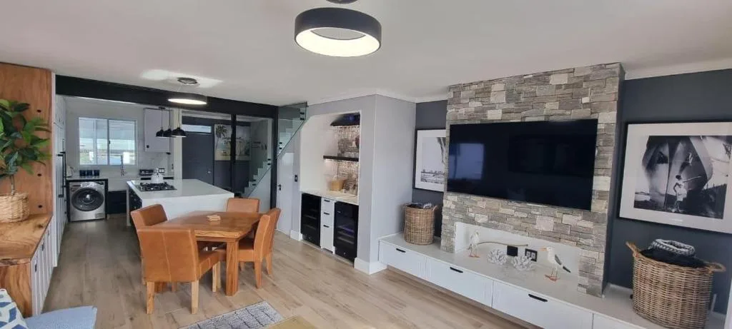 Modern living room with TV, stone fireplace, and open-plan kitchen