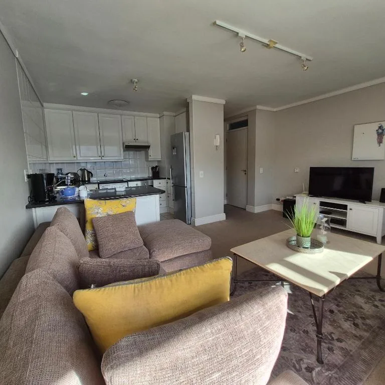 Open-plan living room with grey sofa, TV, and kitchen visible beyond