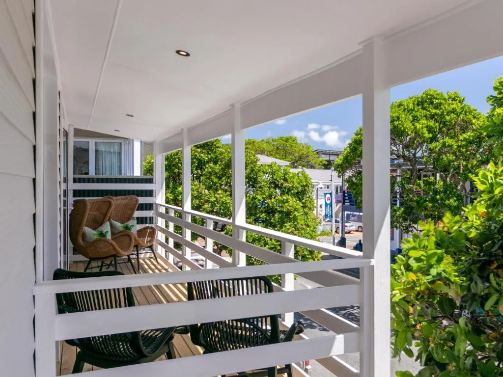 Covered balcony with wicker chairs overlooking lush greenery and street