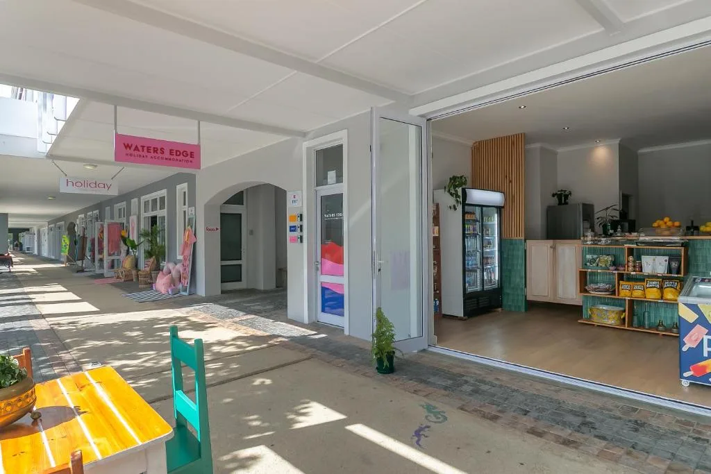 Bright covered walkway with shop fronts and open doors at Waters Edge Knysna