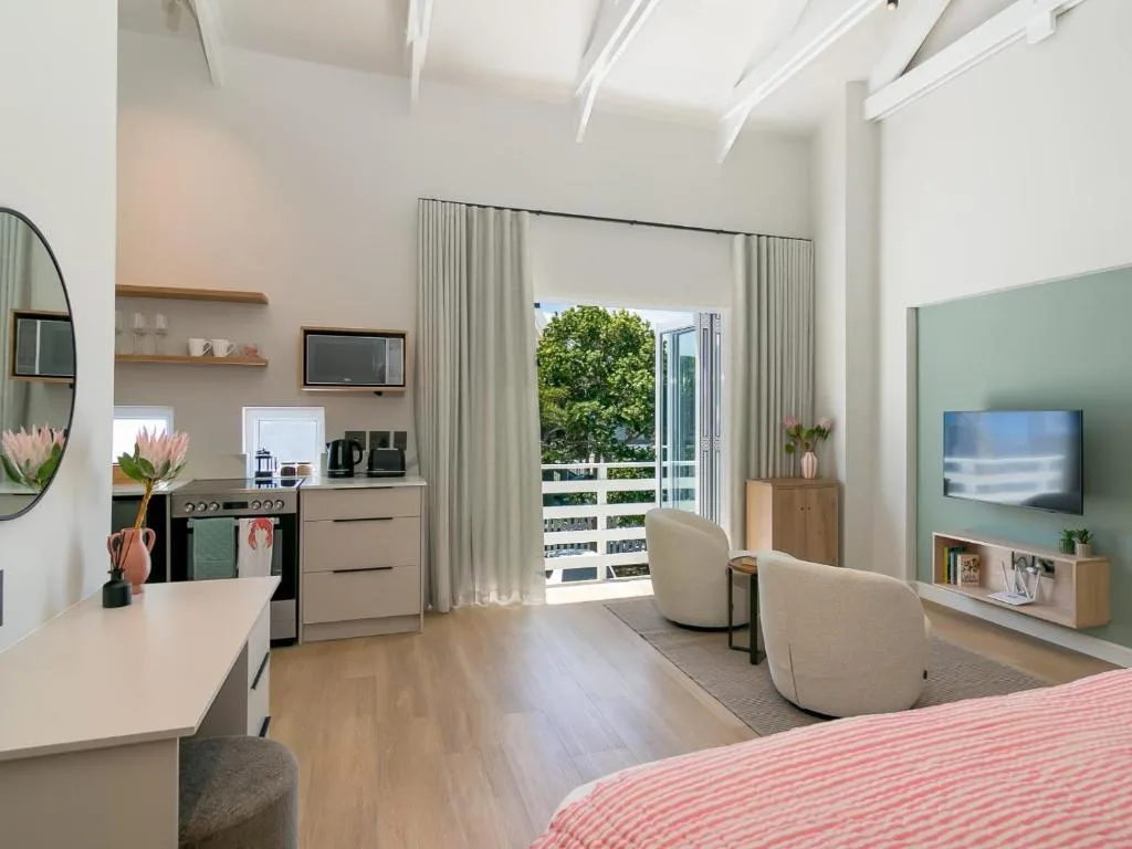 Modern lounge with cream armchairs, TV, and kitchen area with deck access