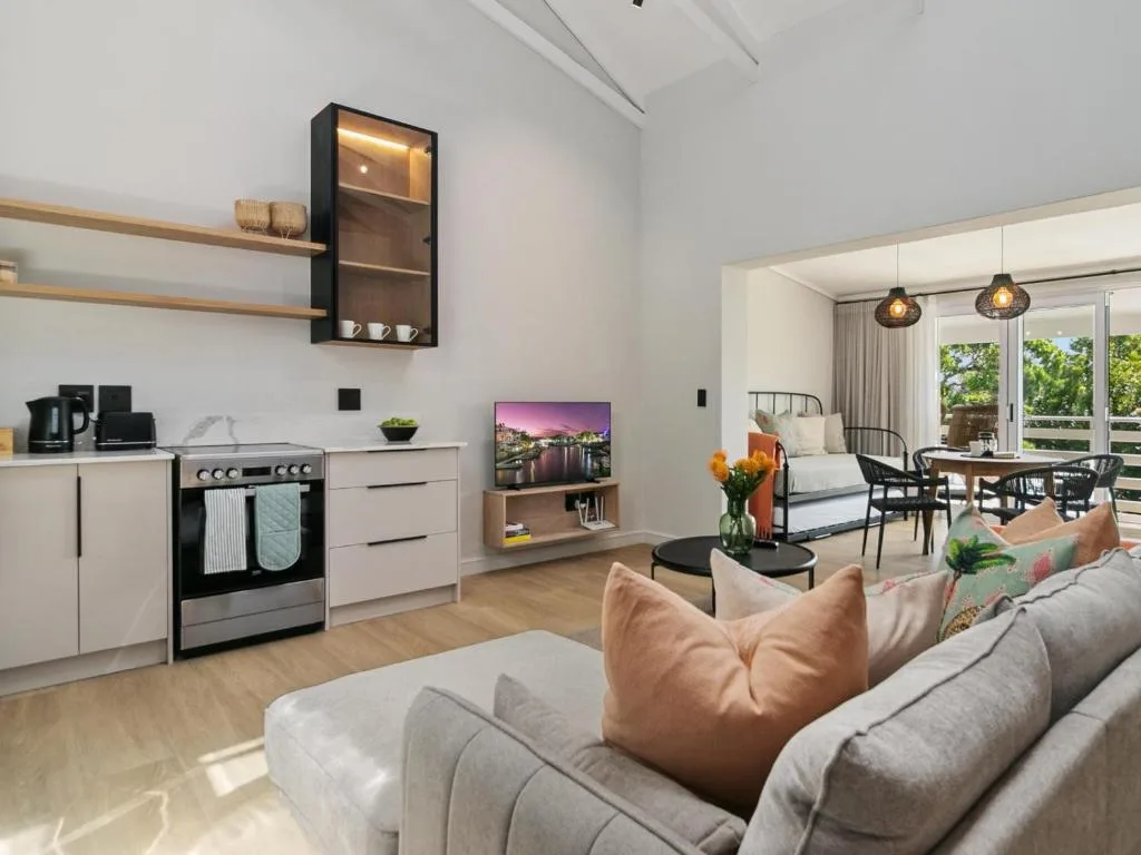 Open-plan lounge with grey sofa, kitchen, and bedroom visible through glass doors