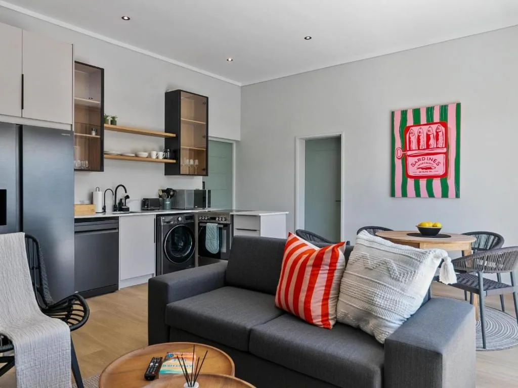 Modern open-plan lounge with dark sofa, kitchen area, and dining space visible