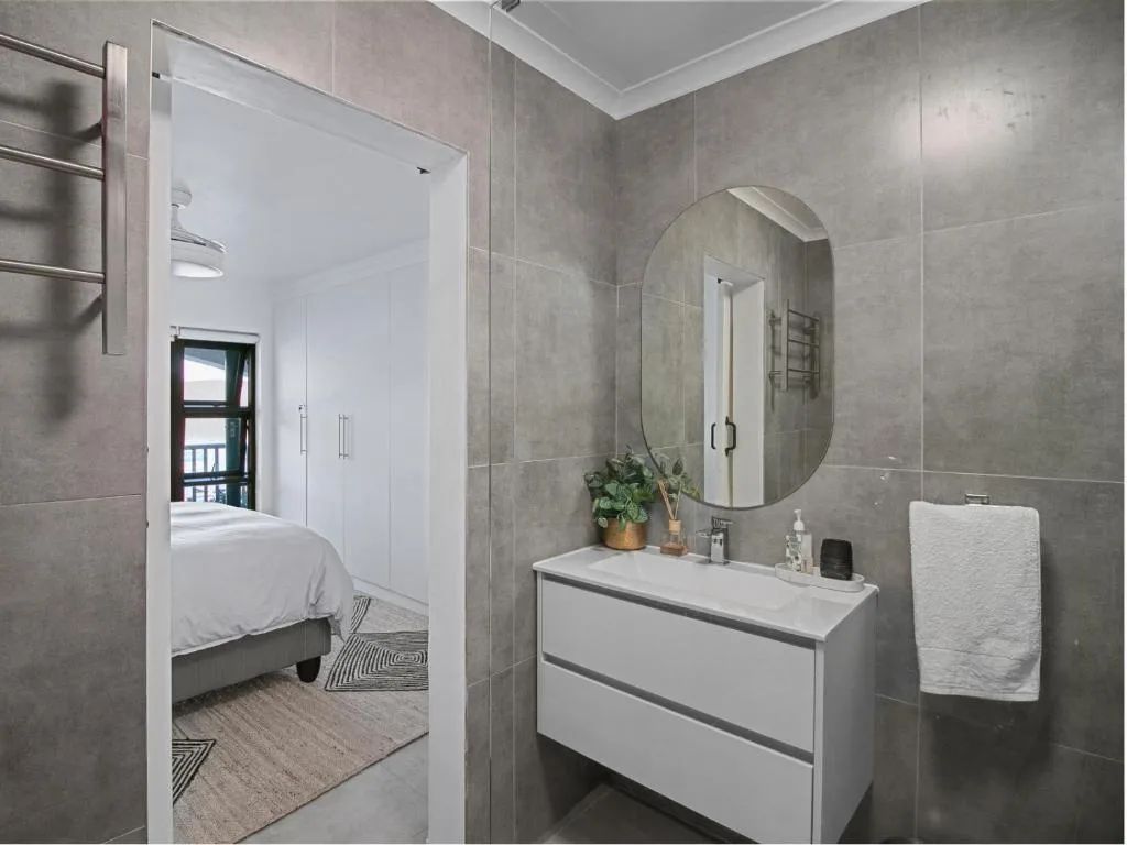 Modern bathroom with grey tile walls, oval mirror, white vanity and towel rail