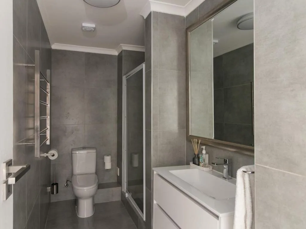 Modern bathroom with gray tile, enclosed shower, vanity sink, and toilet