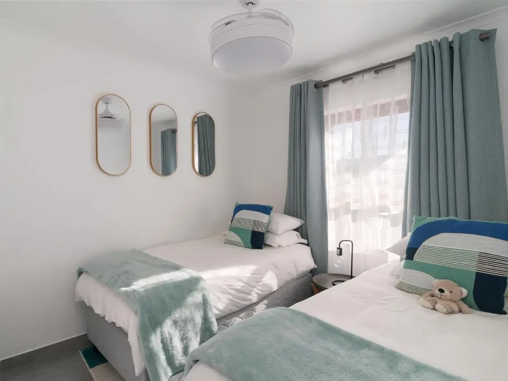 Bright twin bedroom with dual beds, green accents, modern mirrors and natural light