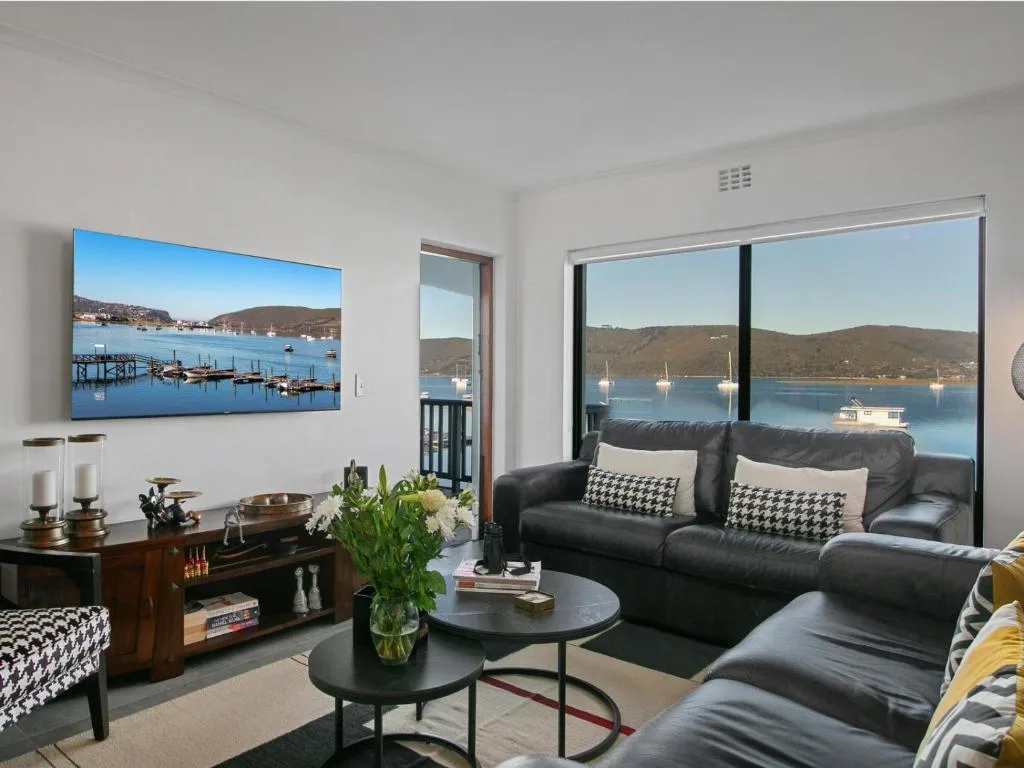 Modern lounge with black leather sofa overlooking Knysna Lagoon through large windows