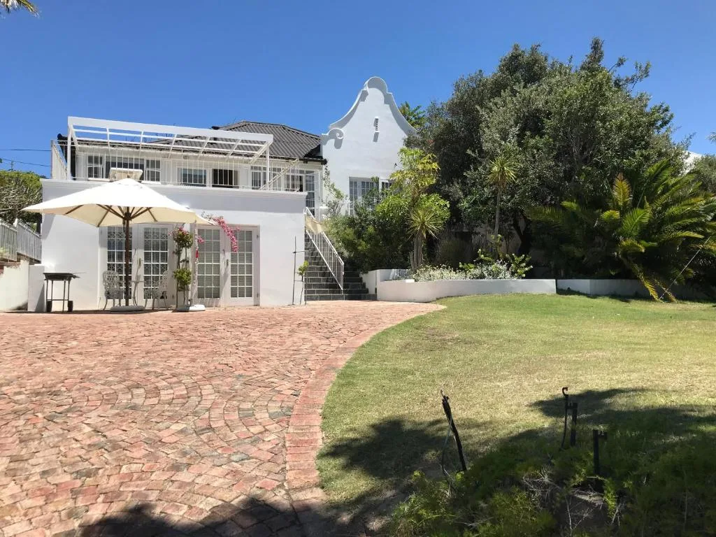 White Cape Dutch-style home with manicured lawn and brick patio