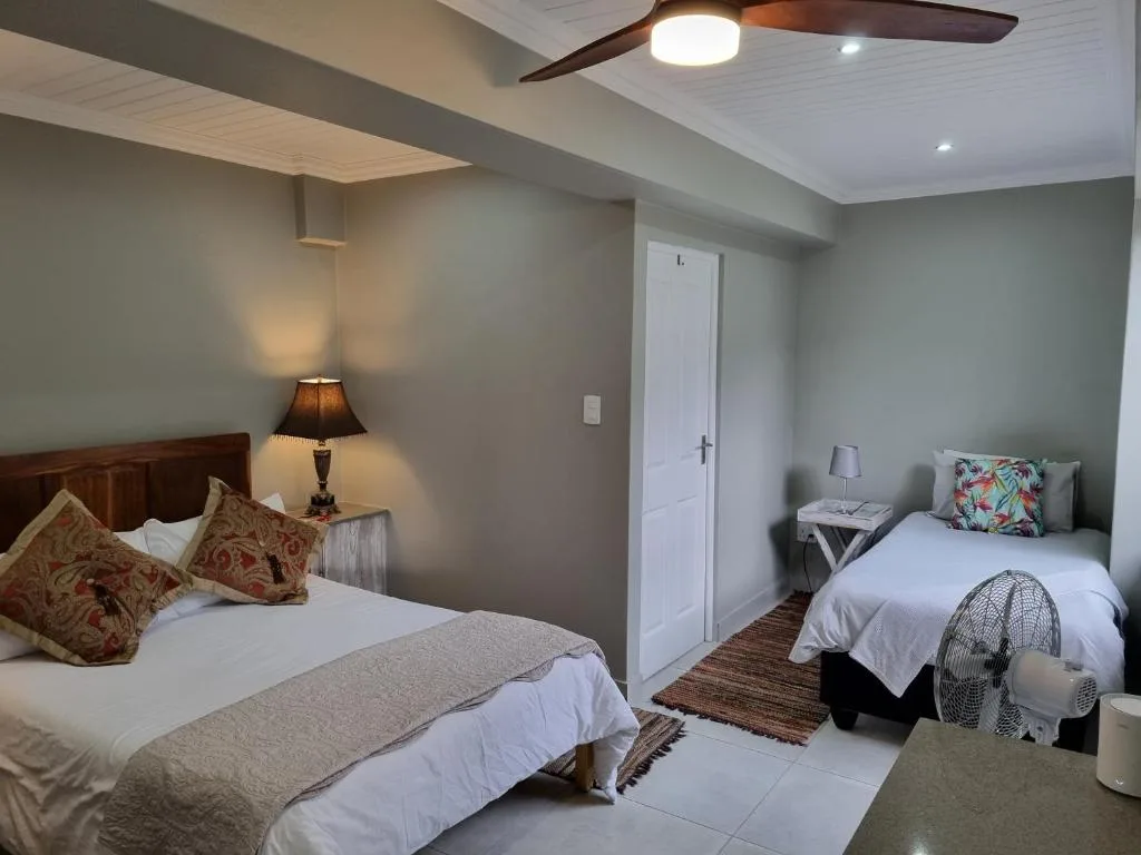 Spacious bedroom with two beds, wooden headboards, and modern ceiling fan
