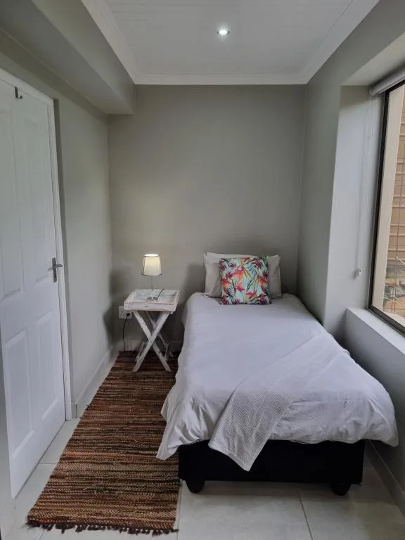 Compact bedroom with single bed, floral cushion, bedside lamp and table