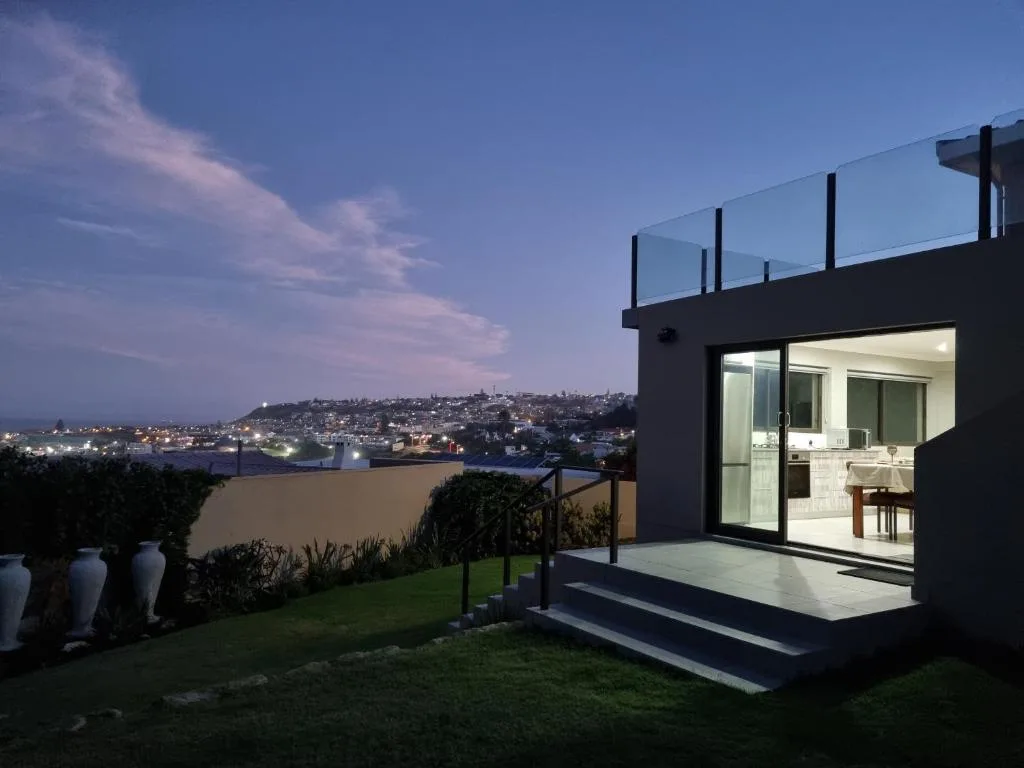 Modern deck with glass railing overlooking illuminated town at dusk