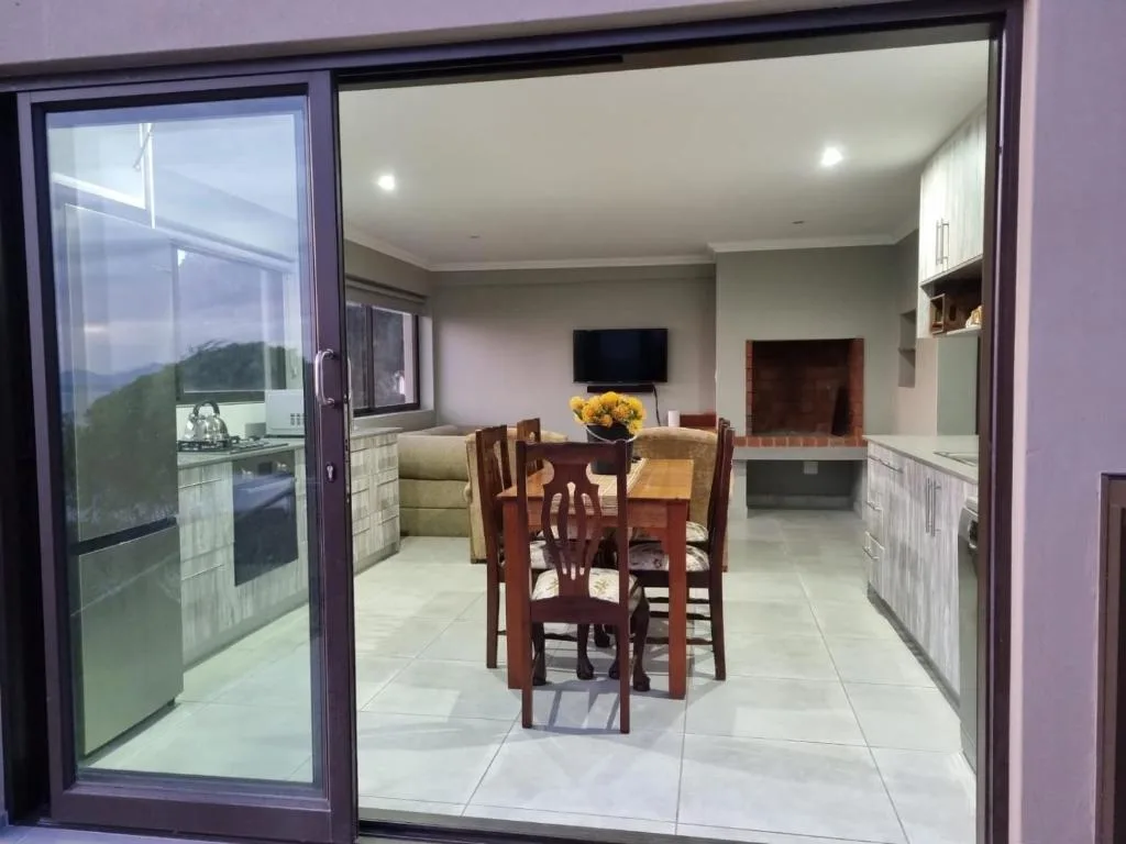 Open-plan dining area with wooden table, chairs, and mountain views through glass doors