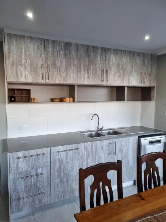 Modern kitchen with grey cabinetry, stainless steel sink, and white countertop
