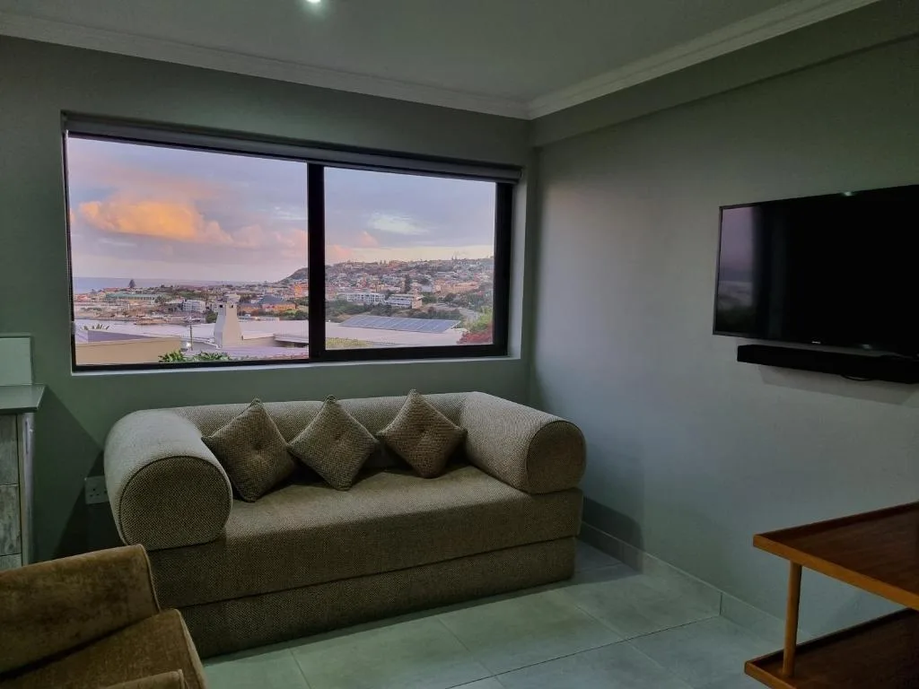 Modern lounge with green sofa, wall-mounted TV, and panoramic coastal views