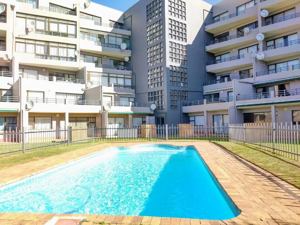 Rectangular swimming pool with turquoise water surrounded by manicured lawn and apartment buildings