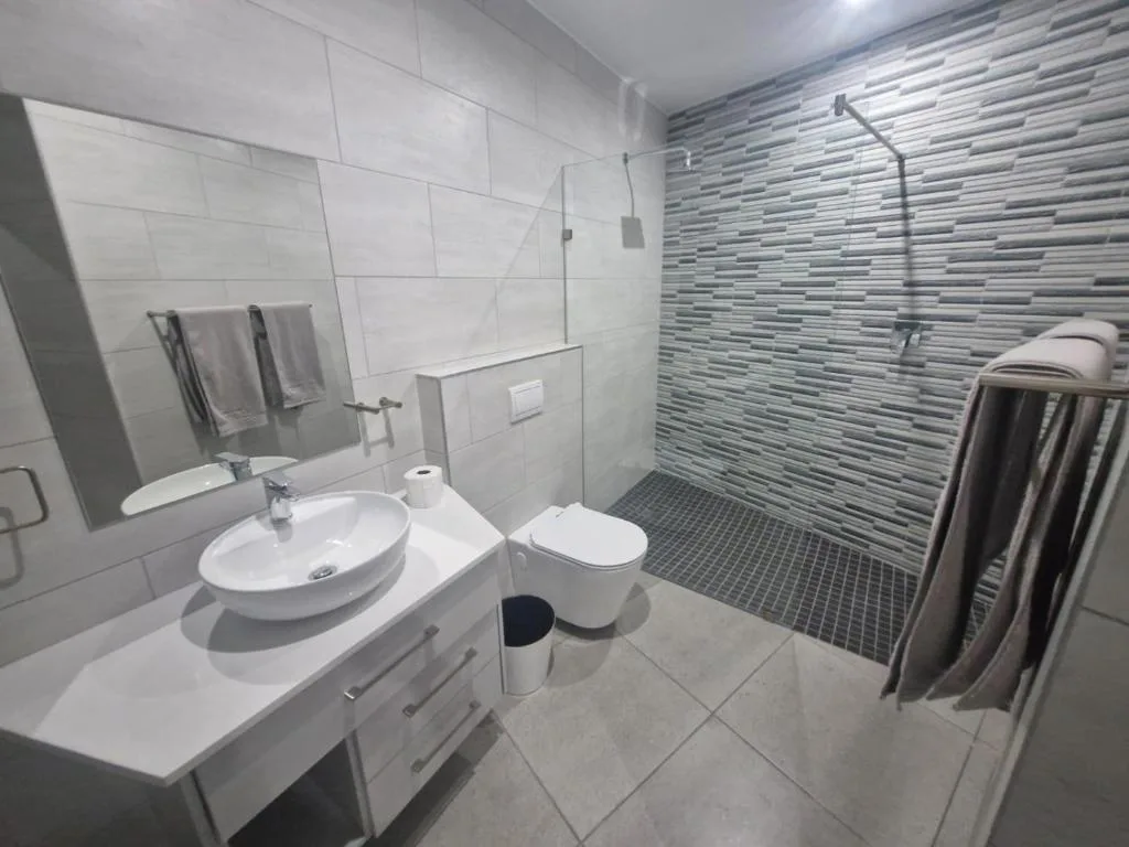 Modern bathroom with round sink, toilet, and walk-in shower with striped tile accent wall