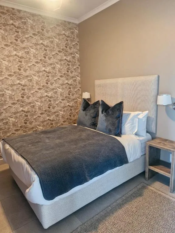 Spacious bedroom with upholstered bed, dark pillows, and warm beige wallpaper