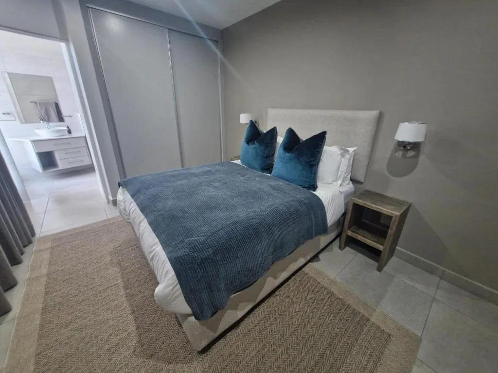 Modern bedroom with queen bed, blue pillows, and ensuite bathroom visible