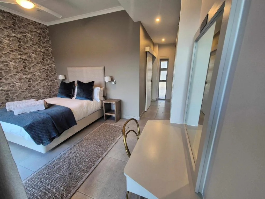 Modern bedroom with queen bed, textured accent wall, and ensuite entrance