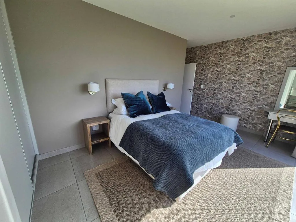 Modern bedroom with queen bed, blue bedding, stone accent wall, and side tables